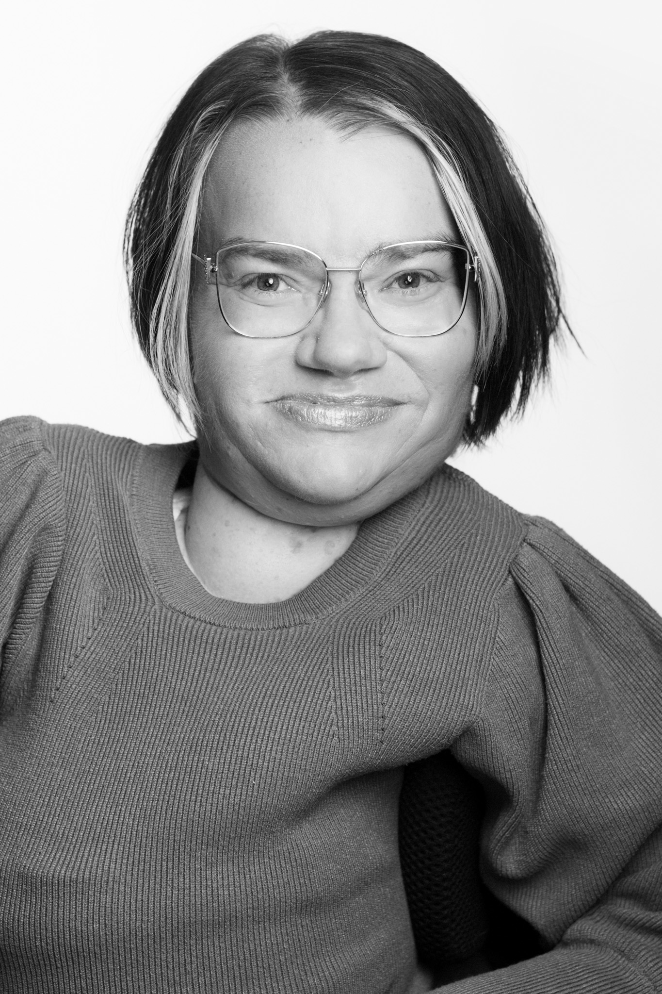 Vit kvinna med mörkt kort hår och några ljusa slingor, samt glasögon.