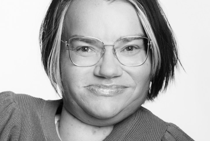 Vit kvinna med mörkt kort hår och några ljusa slingor, samt glasögon.