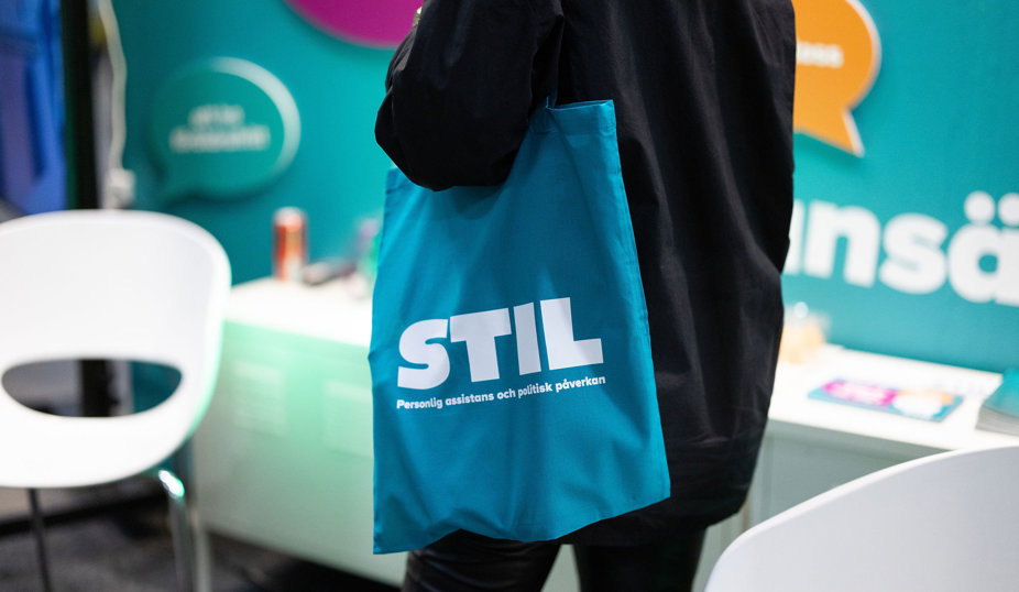 Person bär en turkos tygpåse med texten ’STIL’.
