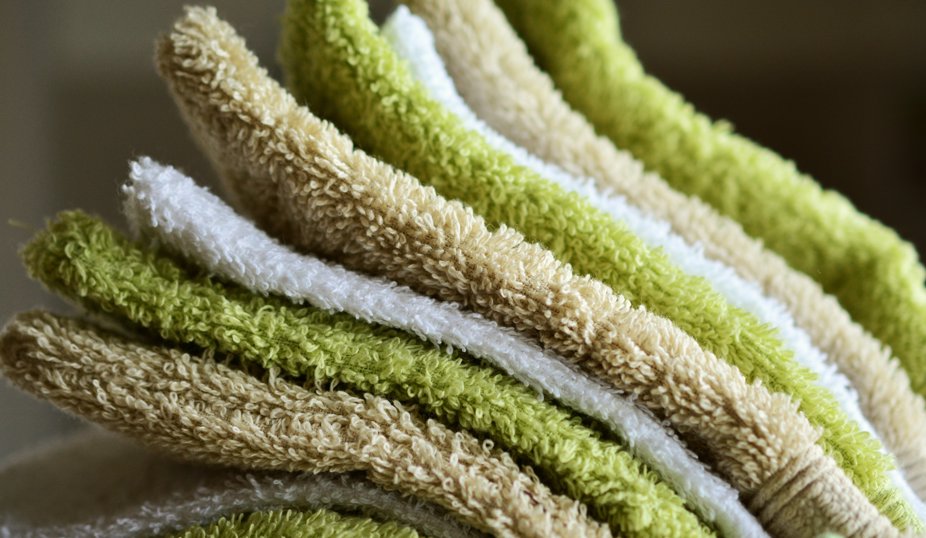 Staplad hög med handdukar i grönt, vitt och beige.