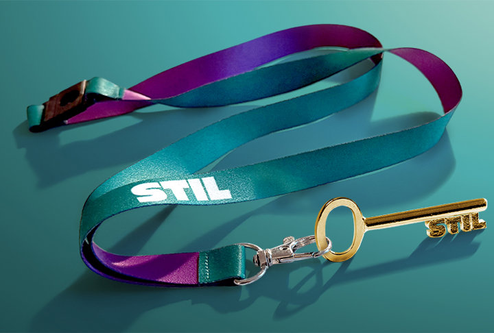 Flerfärgad nyckelrem med texten STIL och en guldfärgad nyckel fäst i en krok.