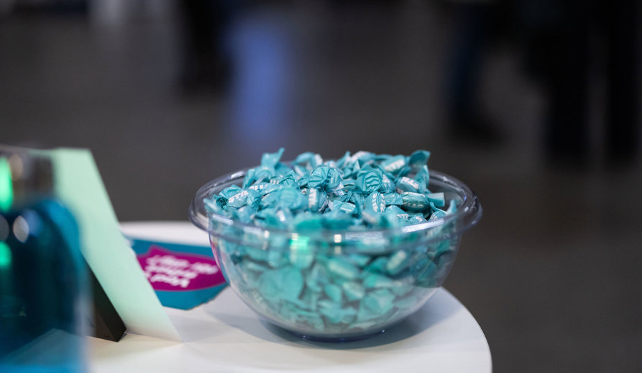 Glasskål fylld med turkosa karameller på ett bord.