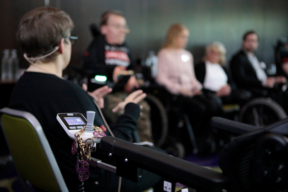 En person i rullstol i förgrunden, omgiven av andra deltagare i ett samtal eller paneldiskussion.
