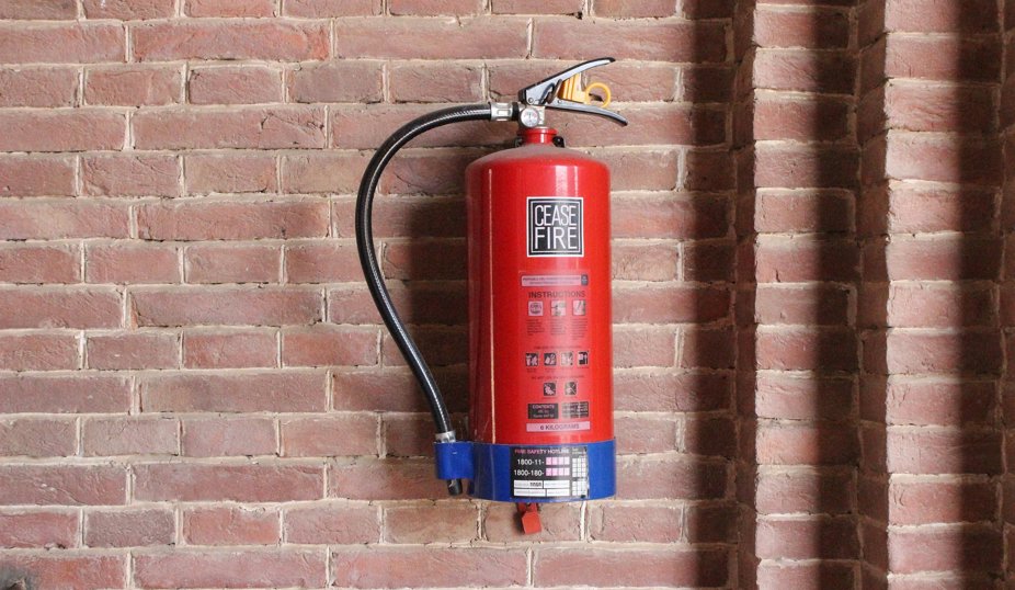 Röd brandsläckare monterad på en tegelvägg.
