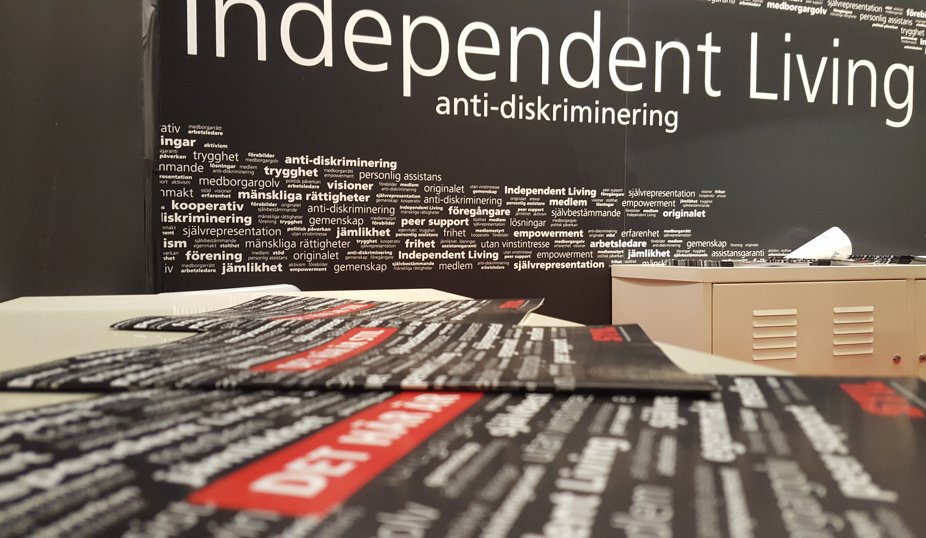 Svart vägg med vita bokstäver. I stort står Independent Living. Framför väggen ett bord med STIL-broschyrer.