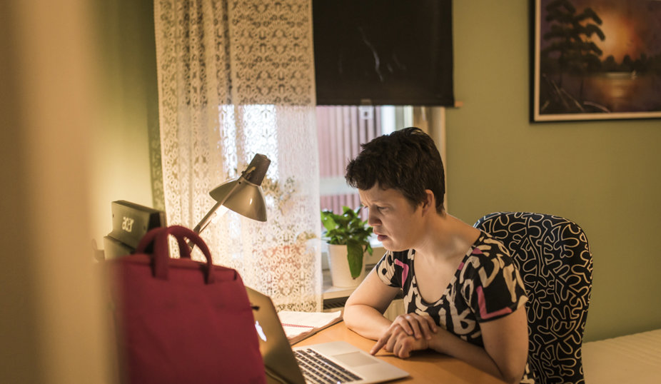 Vit kvinna med kort mörkt hår sitter vid ett skrivbord och jobbar med datorn.