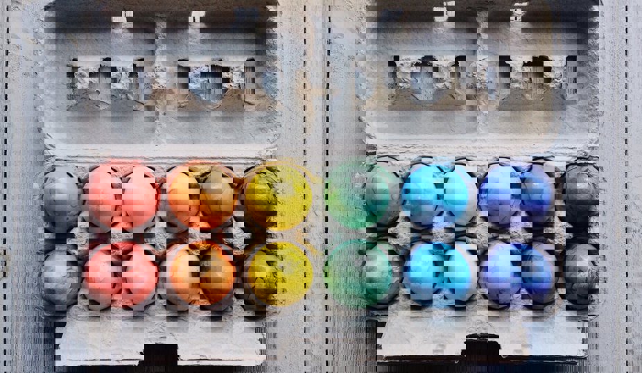 Färgglada målade ägg i en öppen äggkartong, arrangerade i regnbågens färger