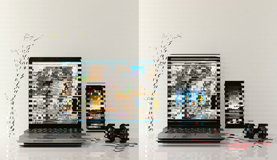 Laptop, surfplatta och hörlurar på ett skrivbord.