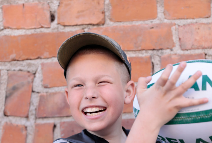 Vit 12-årig kille med ljust hår i rugbyrullstol håller i en rugbyboll.