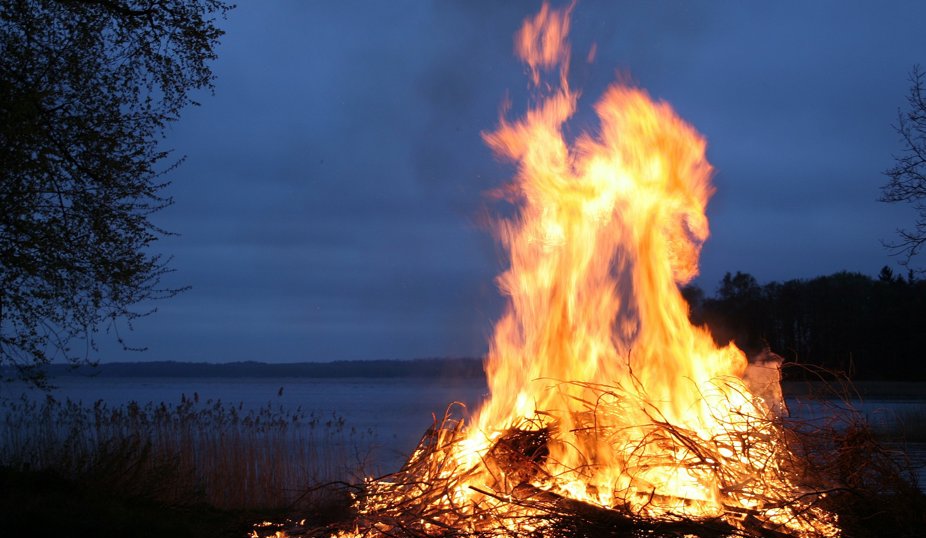 Stor brasa som brinner vid en sjö i skymningen.